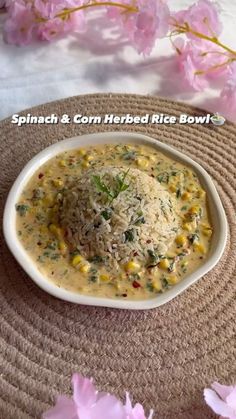 a bowl filled with rice and corn on top of a mat next to pink flowers