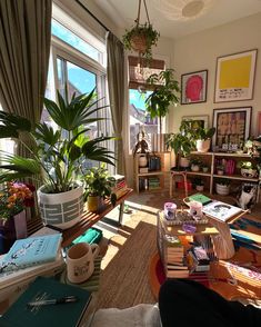 a living room filled with lots of plants and books on top of a wooden table