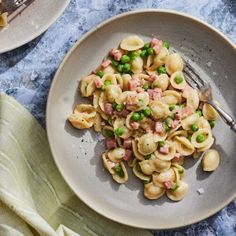 a plate with pasta, peas and ham on it next to a fork in the bowl