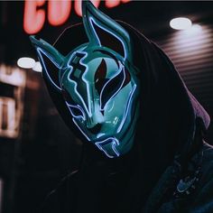 a man wearing a neon mask and hoodie in front of a neon light sign