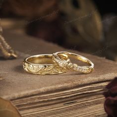 two gold wedding rings sitting on top of an old book