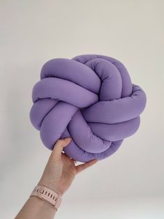 a hand holding up a purple knot cushion