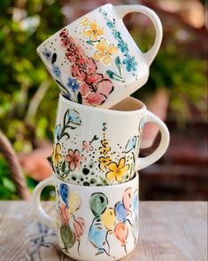 three coffee mugs are stacked on top of each other with flowers painted on them