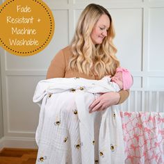 a woman holding a baby wrapped in a white and pink blanket with bees on it