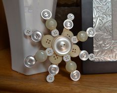 a white vase sitting on top of a wooden table next to a buttoned snowflake