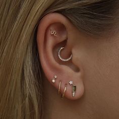 a woman wearing three different ear piercings on her left ear and the other two are gold