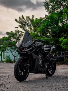 a black motorcycle parked on top of a dirt road next to trees and bushes with clouds in the background