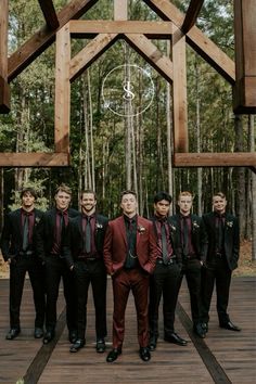 a group of men standing next to each other in front of a wooden structure with trees