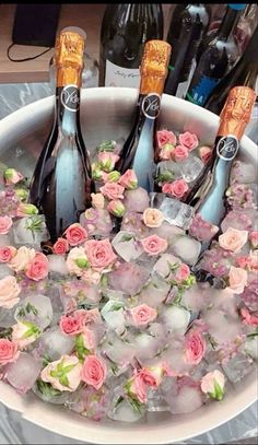 three bottles of champagne are in an ice bucket with pink flowers and roses on it