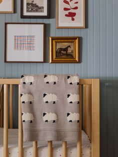 a baby's crib with pictures on the wall and sheep blanket in it