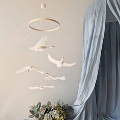 a white bird mobile hanging from a curtain next to a vase with flowers in it