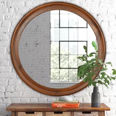 a round mirror on a brick wall above a wooden table with two drawers and a potted plant