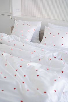 a bed with white sheets and red hearts on the comforter is pictured in this image