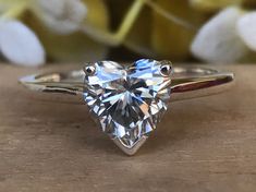 a heart shaped diamond ring sitting on top of a wooden table