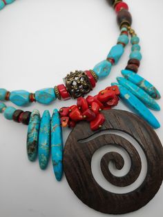 Beautiful ethnic style choker necklace, handmade with various materials: howlite, coral, jasper, hematite, wood. The central element of the necklace is a large pendant made of dark walnut-coloured cut-out wood. The turquoise blue of the jasper and the red of the coral contrast with each other and create a beautiful color combination. The necklace is double stranded, made up of different pearls and shells that create intersections of beautiful shapes and colors. The necklace is rigid but at the same time adheres perfectly to the neck and has an adjustable closure with a 7 cm extension. The necklace is very showy and colourful, in the colors of blue, red and brown, it is reminiscent of summer, the sea...suitable for a low-cut dress for a special occasion. It is a unique design created by me Traditional Turquoise Beaded Necklaces With Wooden Beads, Traditional Turquoise Beaded Necklace With Wooden Beads, Traditional Turquoise Necklace With Wooden Beads, Turquoise Wooden Beads Necklace For Festivals, Bohemian Turquoise Necklace With Wooden Beads, Bohemian Beaded Necklaces With Red Coral, Spiritual Turquoise Necklaces With Wooden Beads, Spiritual Turquoise Necklace With Wooden Beads, Artisan Turquoise Necklace With Wooden Beads