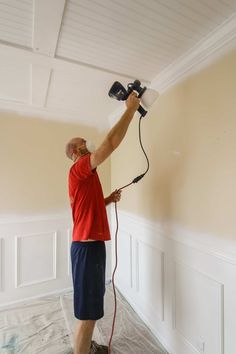 a man is painting the ceiling with a paint roller and a blow dryer in his hand