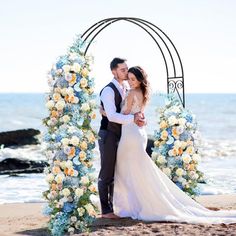 a bride and groom standing under an arch on the beach with flowers in front of them