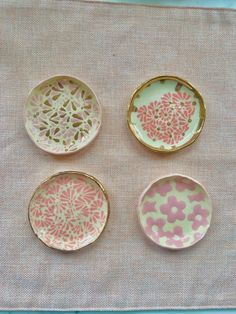 four small plates with designs on them sitting on a cloth covered place mat, one is pink and the other is green