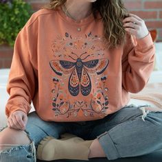 Indulge in the warmth and charm of our cozy sweatshirt featuring a captivating Scandinavian folk-art-inspired moth illustration. Crafted with comfort in mind, this unique and stylish piece effortlessly combines snug vibes with a touch of Nordic whimsy, making it a must-have for those who crave both comfort and distinctive style. The Comfort Colors 1555 sweatshirt offers a relaxed and laid-back fit, providing a comfortable and effortlessly cool look. Its loose silhouette and soft fabric make it t Cottagecore Cotton Sweater For Fall, Fall Cottagecore Crew Neck Sweatshirt, Spring Bohemian Cotton Sweatshirt, Bohemian Cotton Sweater For Fall, Cotton Cottagecore Sweatshirt With Long Sleeves, Cottagecore Long Sleeve Cotton Sweatshirt, Bohemian Crew Neck Sweatshirt For Fall, Bohemian Relaxed Fit Sweatshirt For Fall, Bohemian Cotton Sweater Relaxed Fit