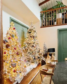 two christmas trees are sitting in the middle of a room with green doors and windows