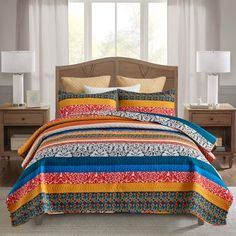 a bed with colorful bedspread and pillows in a room next to two lamps