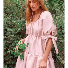 a woman in a pink dress standing next to bushes