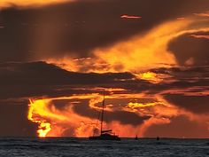 the sun is setting over the ocean with boats in the foreground and clouds in the background