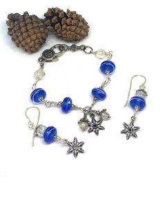 a bracelet with blue beads and silver charms on it, next to a pine cone