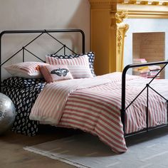 a bed with pink and white striped comforter next to a fire place in a room