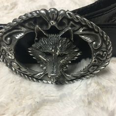 a metal belt with an animal head on it's side, sitting on a white fur surface