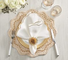 a white and gold place setting with silverware, napkins and flowers on the table