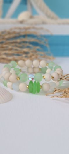 three bracelets with green and white beads sitting on a table next to seashells