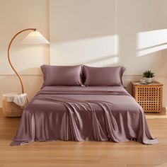 a bed with purple sheets and pillows in a room next to a wooden floor lamp