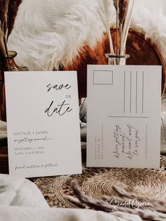 two wedding cards sitting on top of a bed next to each other with feathers in the background