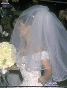 the bride is walking down the aisle with her veil over her head and flowers in her hand