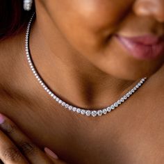 a close up of a woman wearing a diamond necklace and bracelet with her hand on her chest