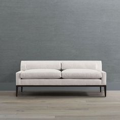 a white couch sitting on top of a hard wood floor next to a gray wall