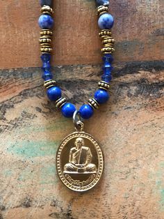 I hand crafted this one-of-a-kind necklace with a Buddhist amulet pendant, and blue natural stone, glass, and gold tone metallic beads.  The pendant is a Buddhist amulet from Thailand, depicting a revered Thai Buddhist monk on the front and a message in Thai on the back.  This amulet has been blessed by a Thai Buddhist monk.  The necklace measures 22 inches long, with an additional 1.25 inches for the pendant.  It has a toggle clasp. Ours is a non-smoking home. Spiritual Round Beads Jewelry For Blessing, Spiritual Jewelry With Round Gemstone Pendant, Spiritual Round Pendant With Gemstone Beads, Handmade Amulet Beads For Meditation, Handmade Symbolic Jewelry For Blessing, Spiritual Jewelry With Polished Beads As Gift, Spiritual Healing Medallion Necklace, 8mm Beads Amulet Jewelry For Meditation, Amulet Style Jewelry With 8mm Beads For Meditation