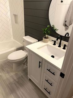 a white toilet sitting next to a bath tub in a bathroom under a round mirror