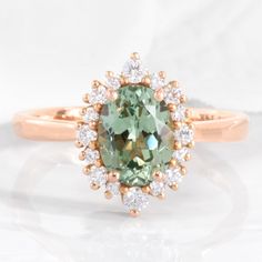 This strikingly gorgeous green sapphire engagement ring features an 8x6mm oval cut conflict free cultured sea foam green sapphire set in our Tiara Halo Diamond ring. The petite band gently tapers toward the green sapphire center surrounded by brilliant white diamonds, creating an elegant feminine curve. This unique oval sapphire and diamond ring is a perfect alternative engagement ring for brides who love one of a kind rings. It can be crafted in your choice of platinum or 14k or 18k yellow, ros Olive Engagement Ring, Oval Ring Band, Halo Oval Ring, Rose Gold Halo Diamond Ring, Sapphire Diamond Engagement Ring, Rose Gold Halo Engagement Ring, Rose Gold Tiara, Oval Sapphire Ring, Green Sapphire Engagement