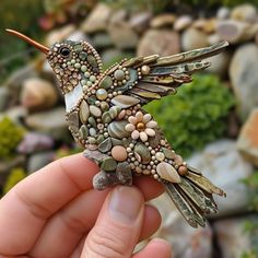 a hand holding a tiny bird made out of beads and stones on it's body