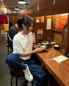 a woman sitting at a table in front of a pan of food with chopsticks