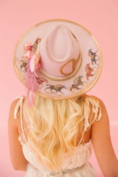 Unleash some playful style with the HORSESHOE PINK RANCHER HAT! This one-of-a-kind hat features a pink color palette with bold gold accents and a cream ribbon band. A racing horses design, gold horse bit patch, and pink floral design add a unique touch, perfect for an unforgettable Derby look. Giddy up! This hat is ONE Painted Hats For Women, Derby Dresses And Hats Outfit, Cowboy Hat With Flowers, Custom Cowgirl Hats, Cowgirl Hat Outfit, 70s Cowgirl, Colorful Cowgirl, Aesthetic Hats, Horses Design