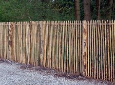 a wooden fence with gravel and trees in the background