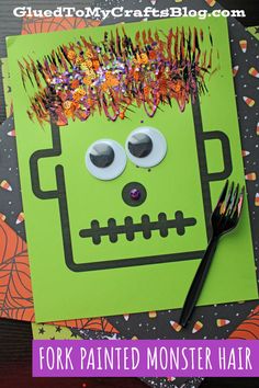 a green monster paper craft with scissors and sprinkles on it, sitting next to a fork