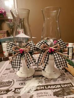 two white ceramic vases with bows on top of newspaper paper next to each other