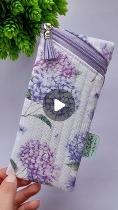 a hand holding a purple and white flowered pouch with a video playing on it