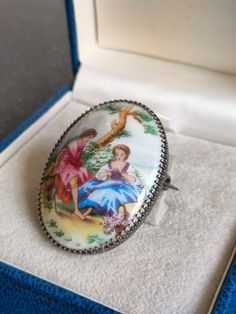 an oval shaped glass ring in a white box with blue trimming and a painting on it