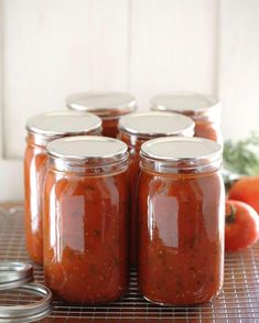 four jars filled with red sauce sitting on top of a wooden table next to tomatoes