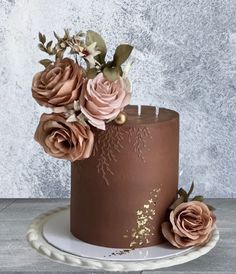 a chocolate cake with pink flowers on top and gold leaf decoration, sitting on a white plate